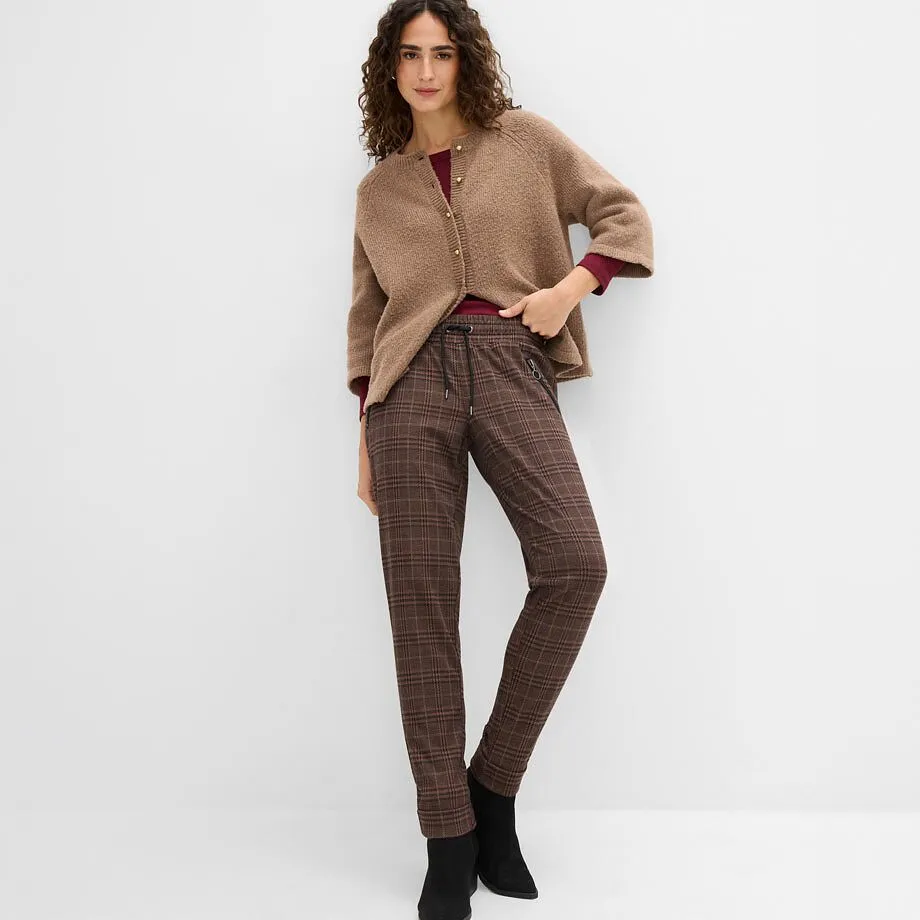 Cardigan marrone, top rosso, pantaloni a quadri e stivaletti neri.