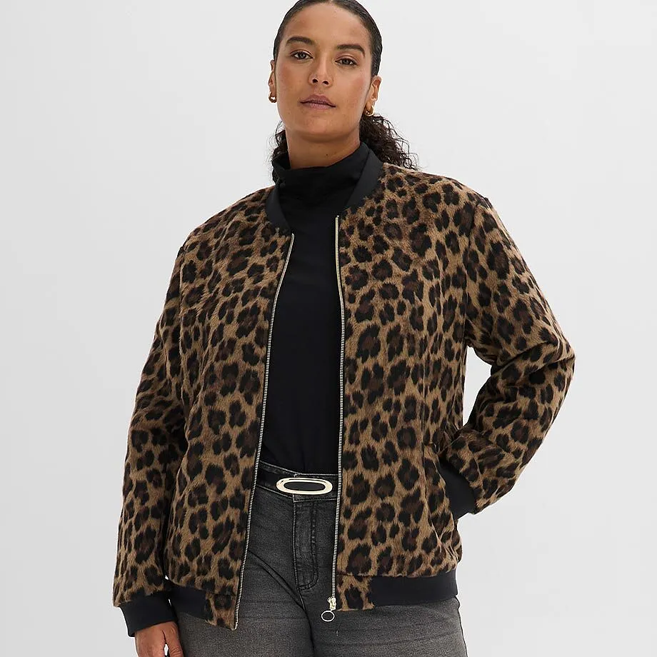 Giacca bomber leopardata sopra un dolcevita nero, abbinata a jeans grigi e a un'elegante cintura.