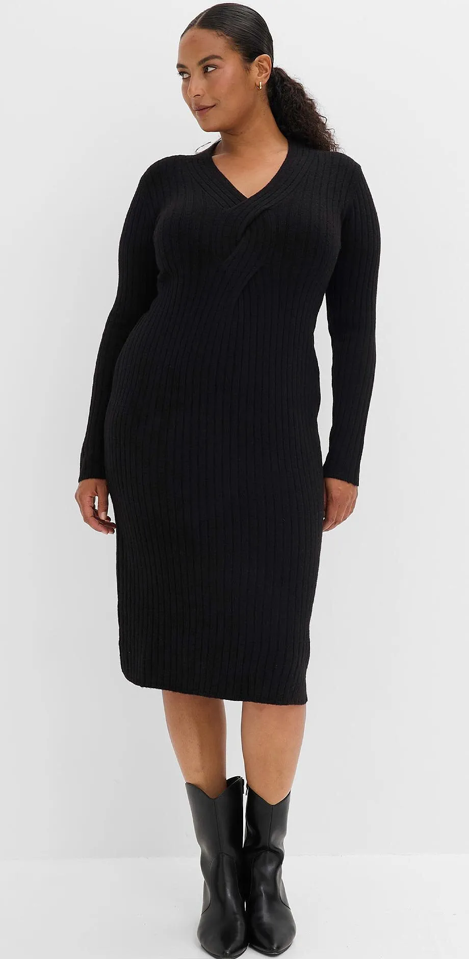 Una donna indossa un elegante abito nero in maglia a coste e stivali neri.
