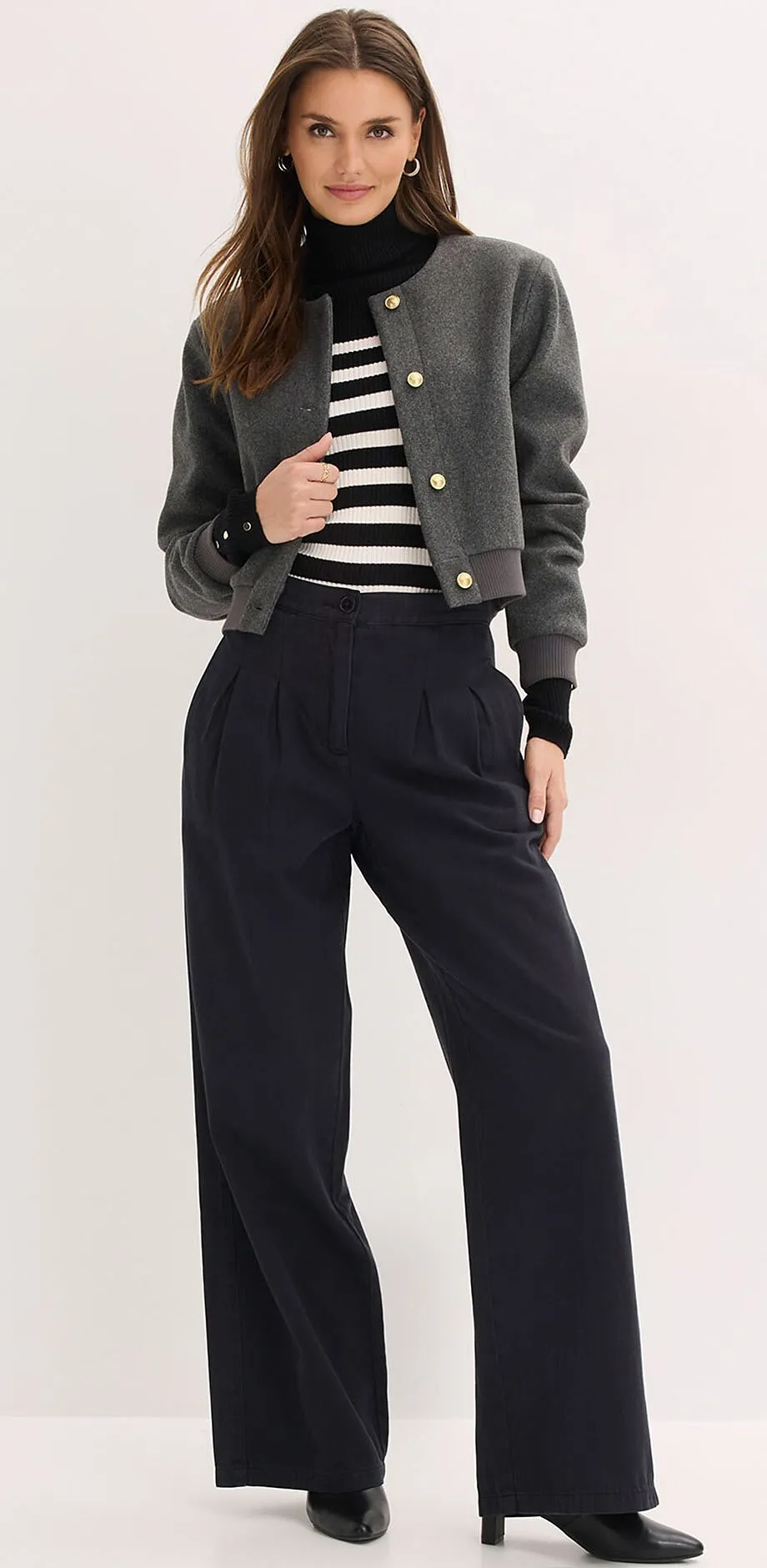 Giacca grigia, maglione a righe e pantaloni larghi neri.