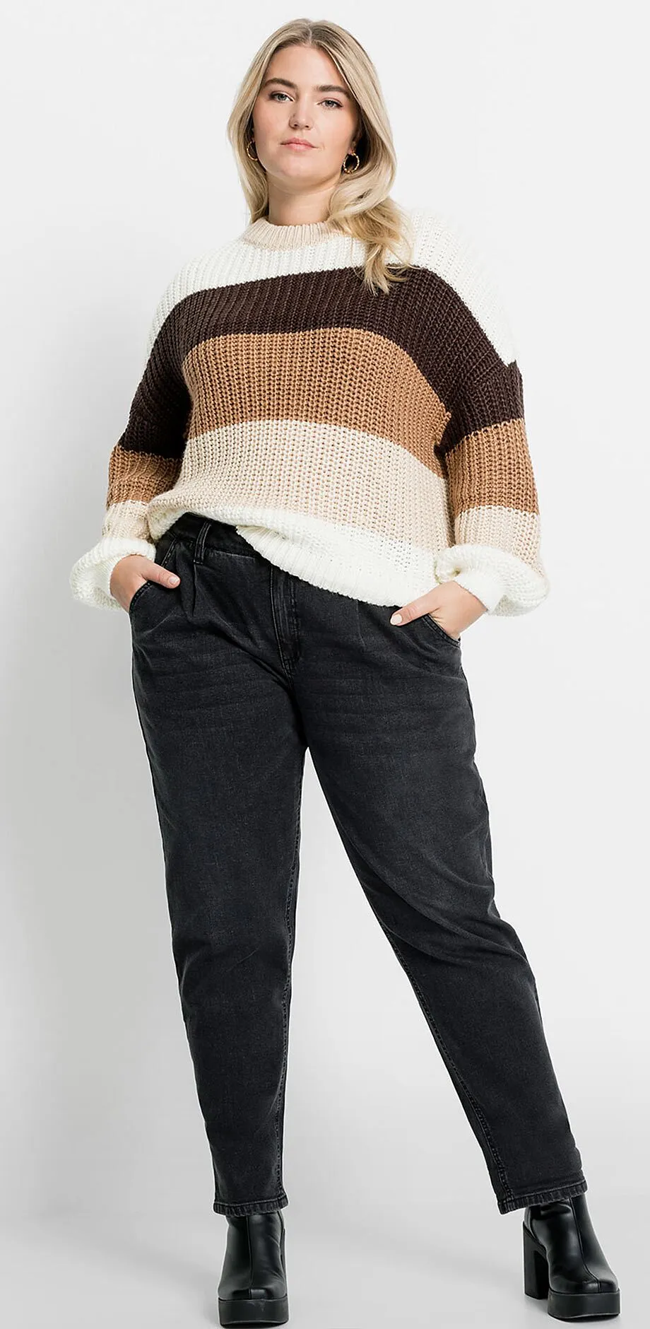 Maglione a righe in tonalit&agrave; terra, abbinato a jeans scuri e scarpe nere.