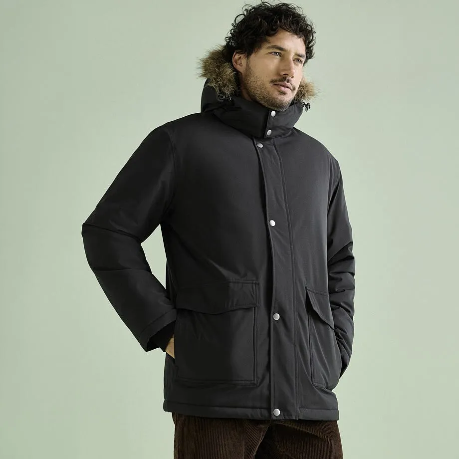 Un uomo indossa un parka invernale nero con cappuccio di pelliccia e pantaloni di velluto a coste marroni.