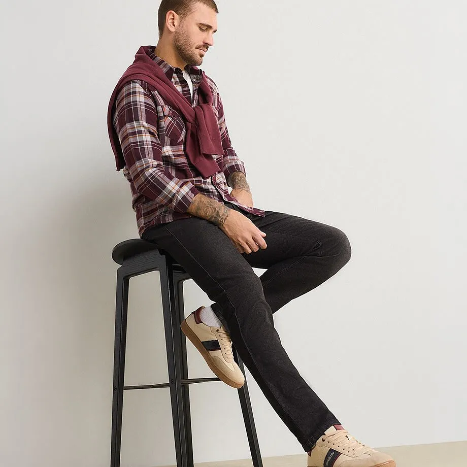 L'uomo indossa una camicia a quadri, jeans scuri, scarpe da ginnastica beige e un maglione color vino.