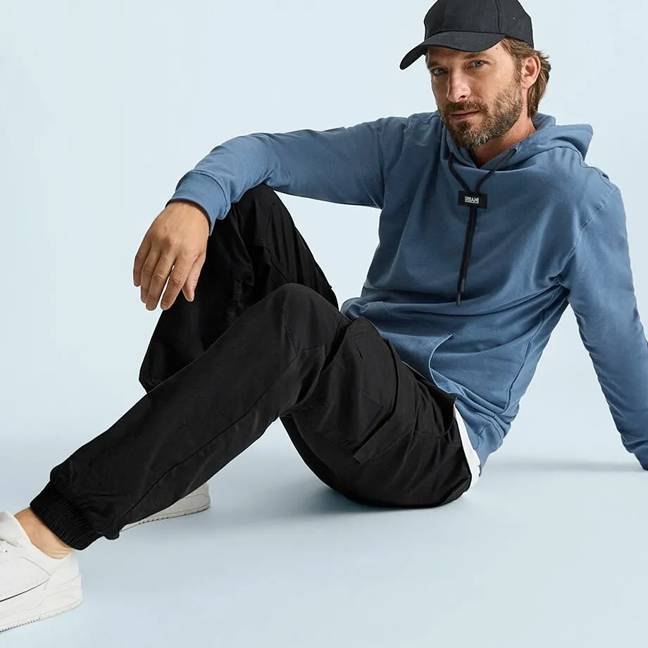L'uomo indossa una felpa blu con cappuccio, pantaloni cargo neri, scarpe da ginnastica bianche e un berretto.