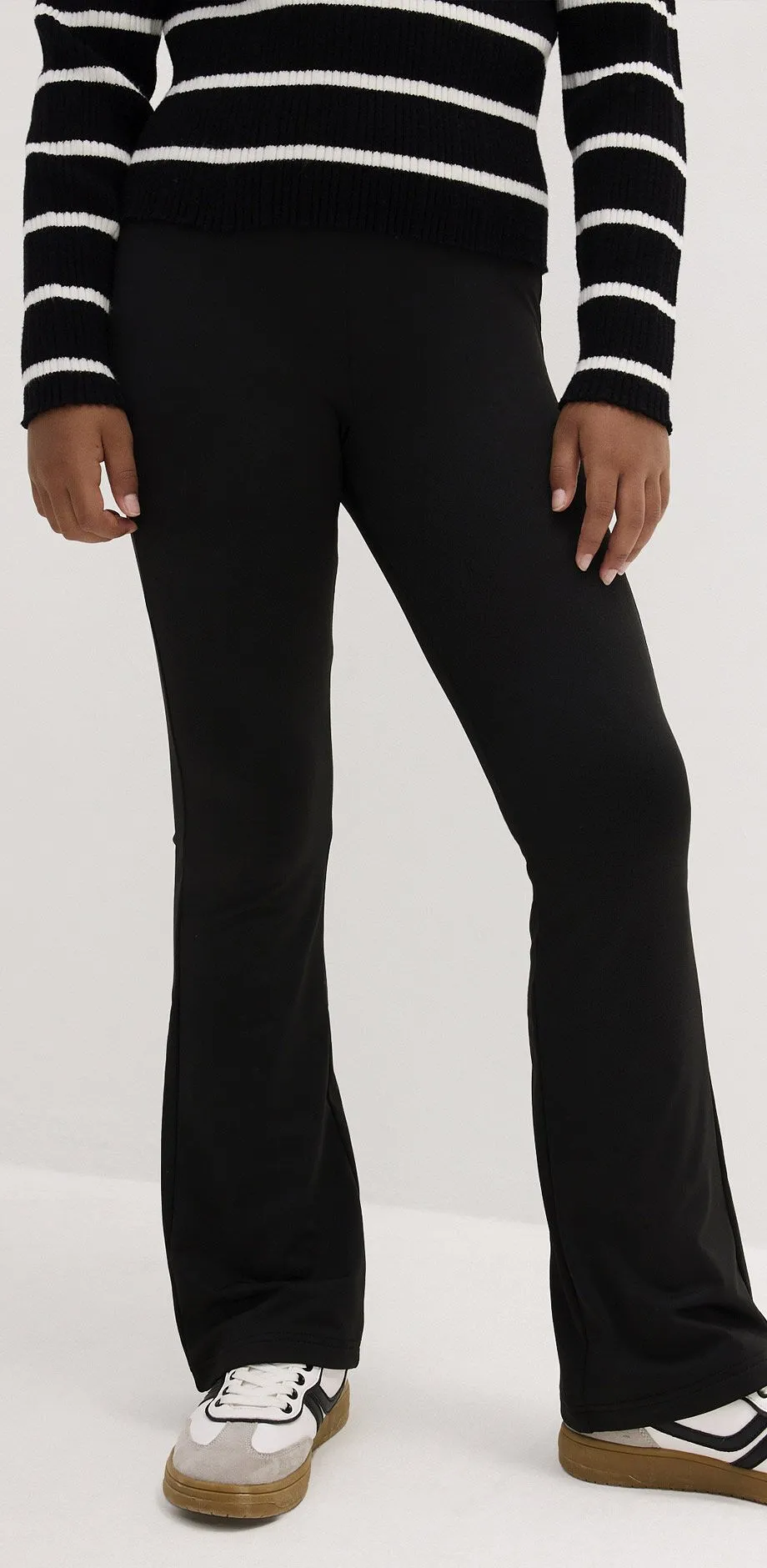 Leggings neri a zampa, abbinati a scarpe da ginnastica bianche e nere e a un maglione a righe