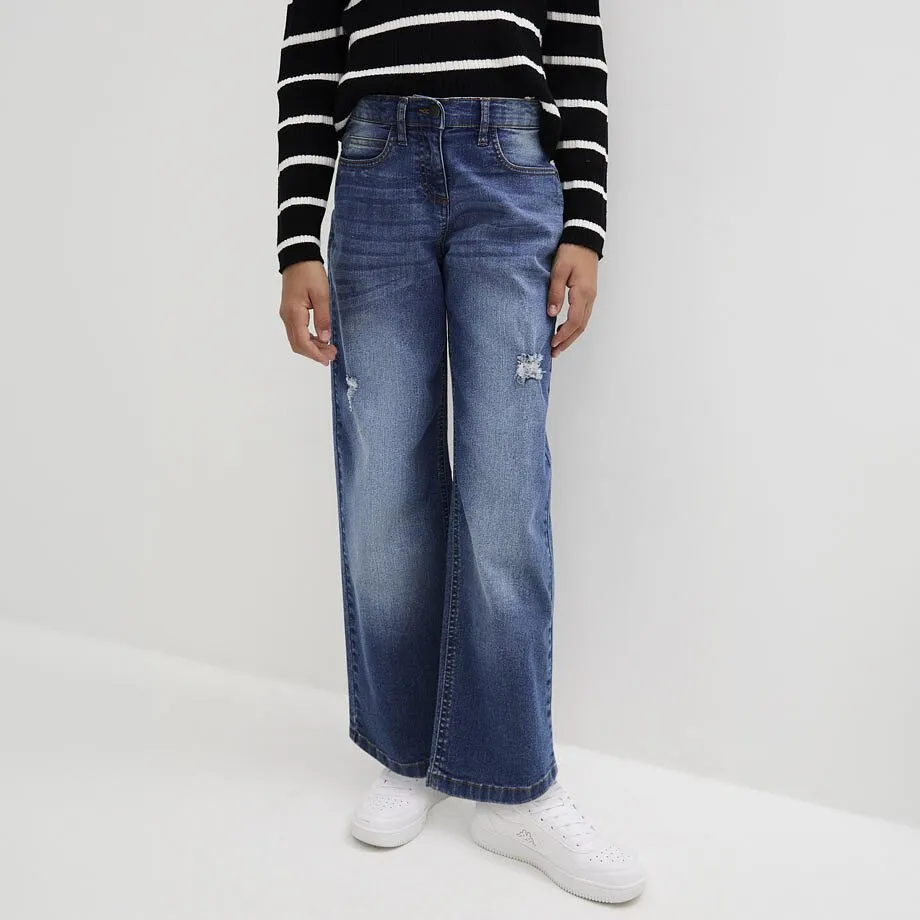 Il bambino indossa una maglietta a righe a maniche lunghe, jeans a zampa blu e scarpe da ginnastica bianche.