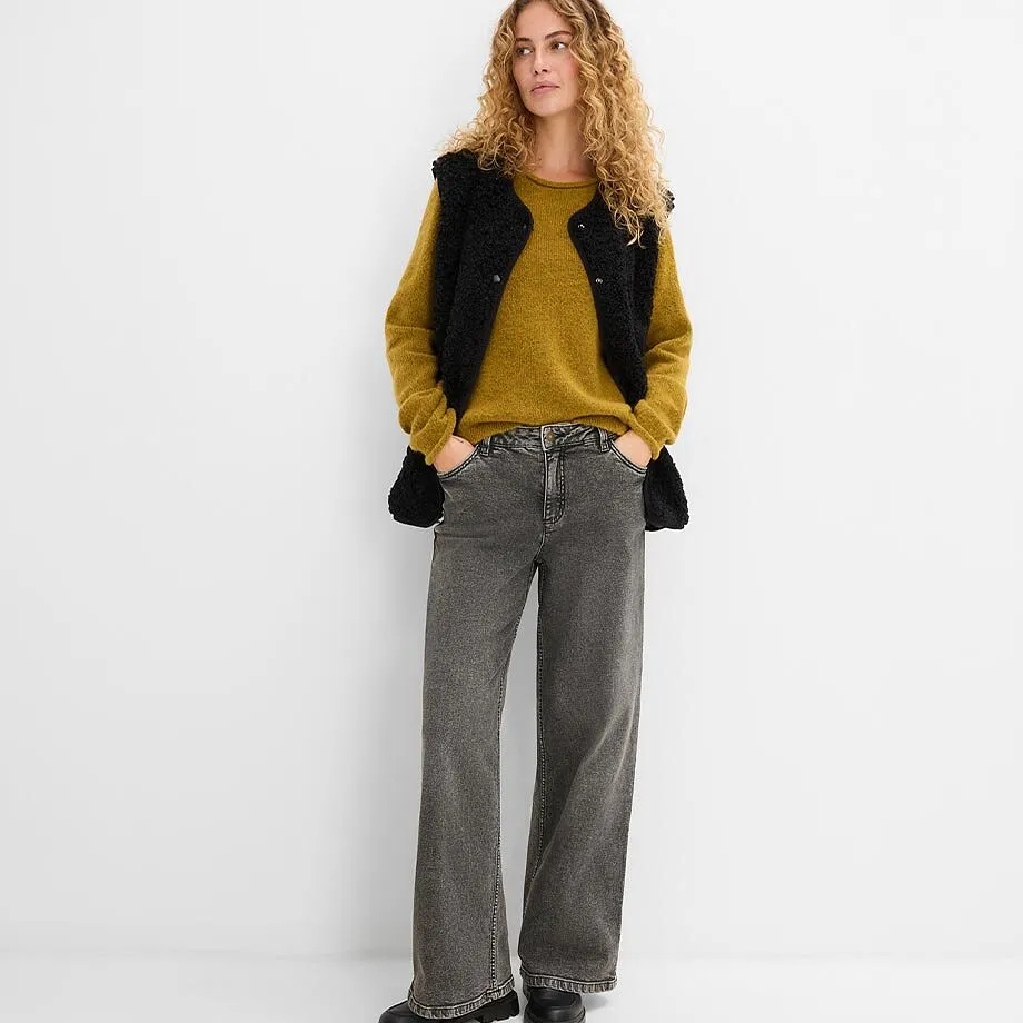 Maglione giallo senape, gilet nero e jeans grigi.
