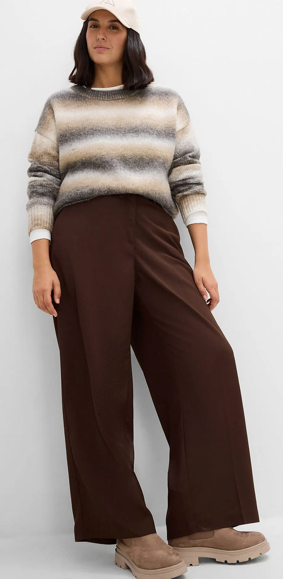 Maglione a righe, pantaloni larghi marroni, comode scarpe con zeppa e un berretto.