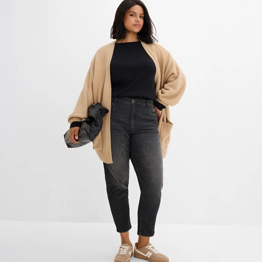 Cardigan lavorato a maglia beige sopra un top nero, abbinato a jeans grigi e sneakers beige.