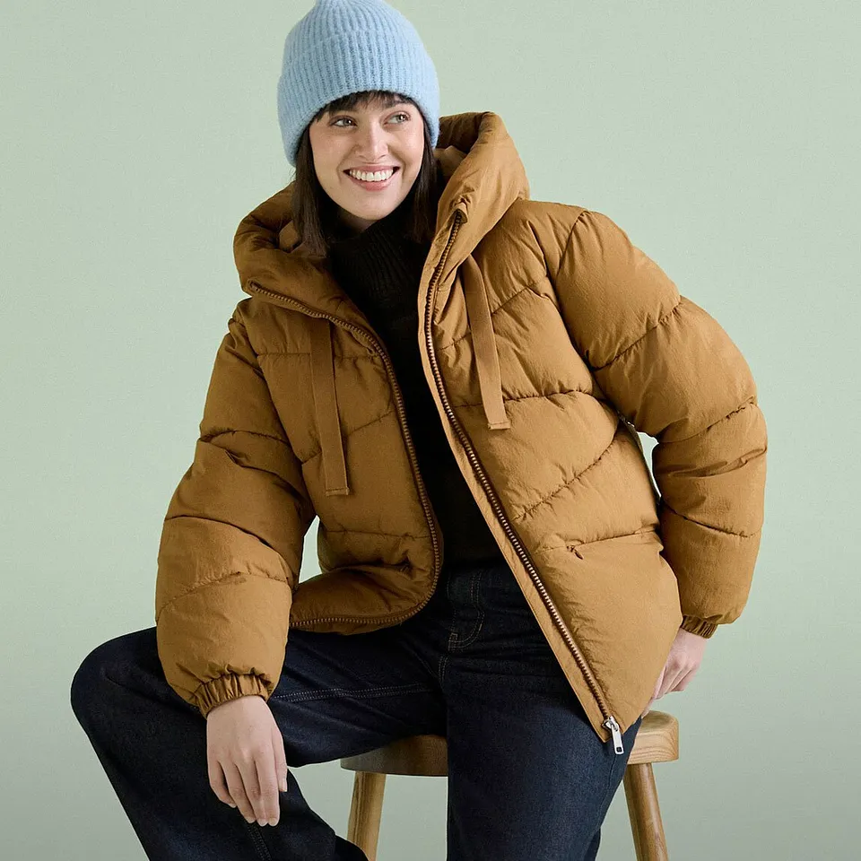 Berretto blu, giacca trapuntata marrone e jeans scuri.