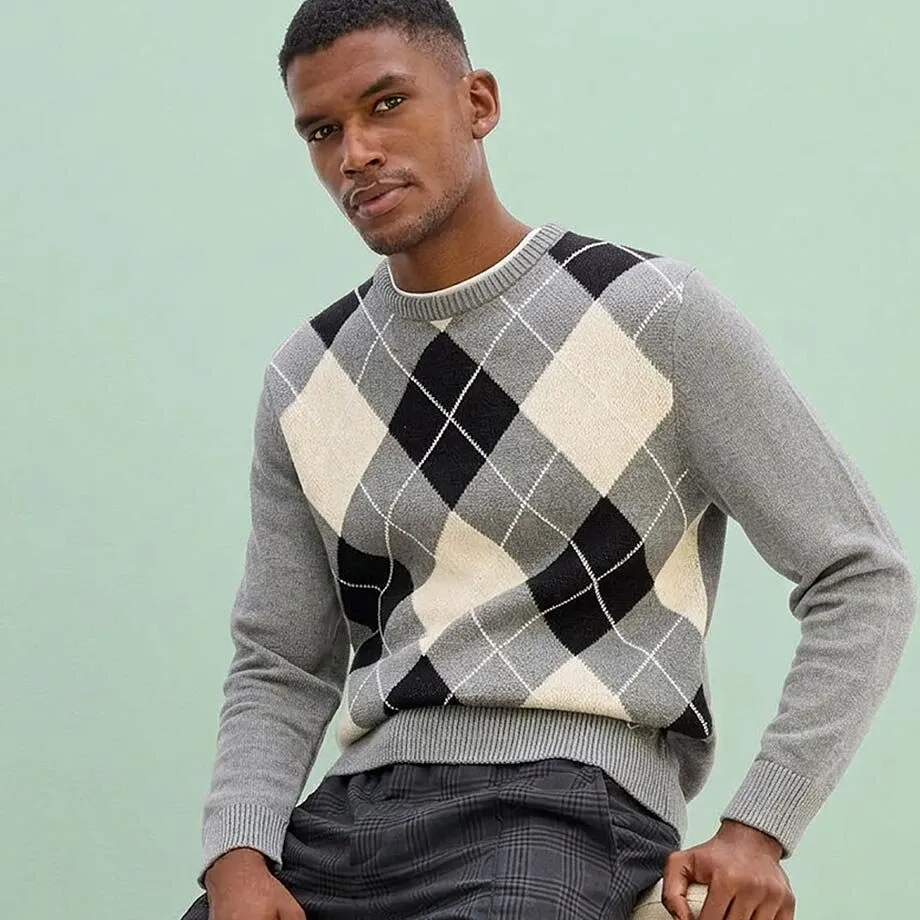 Elegante maglione con motivo Argyle nei toni del grigio, nero e beige, abbinato a pantaloni a quadri.