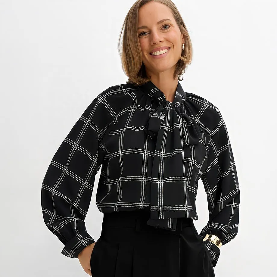 Elegante camicetta nera a quadri con fiocco, pantaloni neri, bracciale dorato.