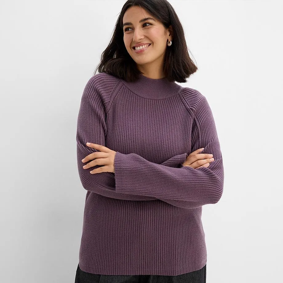 Un maglione viola a coste con collo alto e pantaloni scuri.