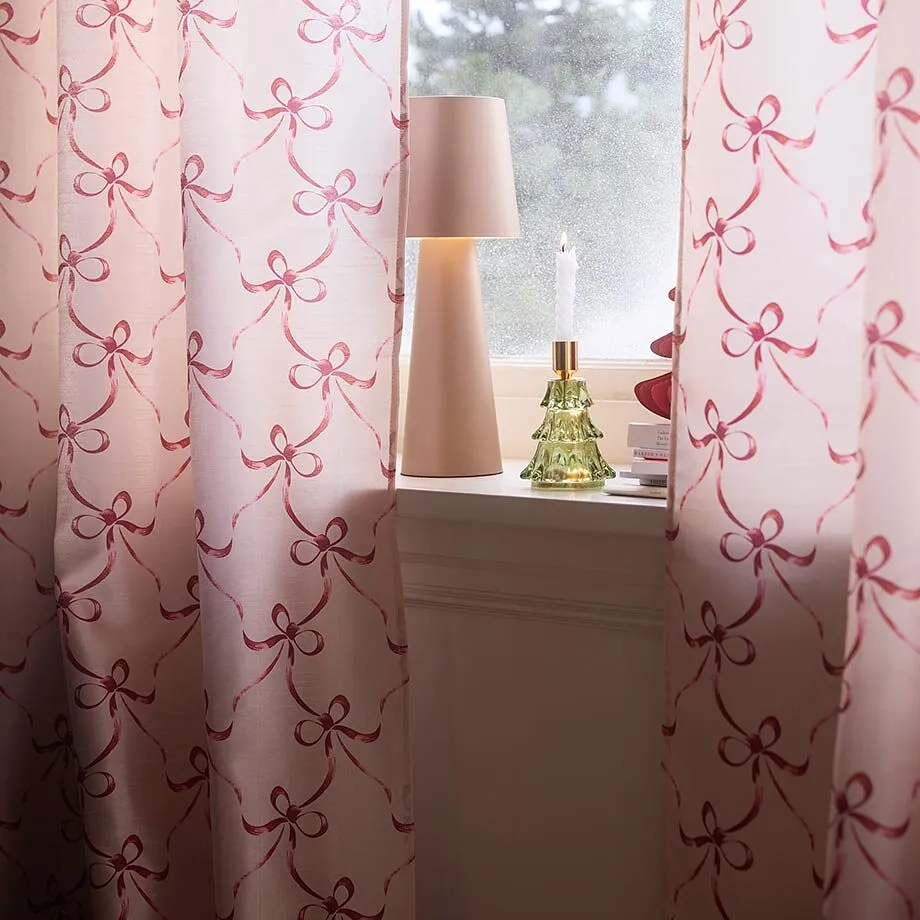 Tende rosa con motivi a fiocchi adornano la finestra insieme alla lampada e alla candela.
