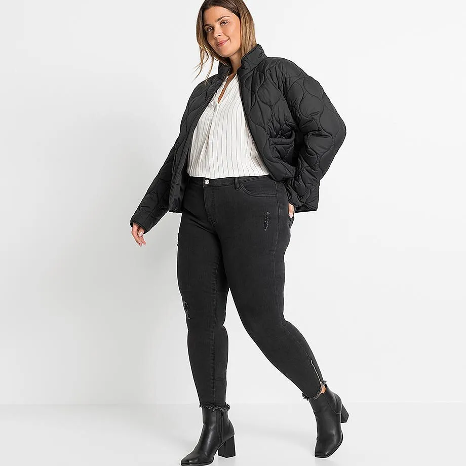 Giacca trapuntata nera, camicetta a righe, jeans con cerniere e stivaletti casual.