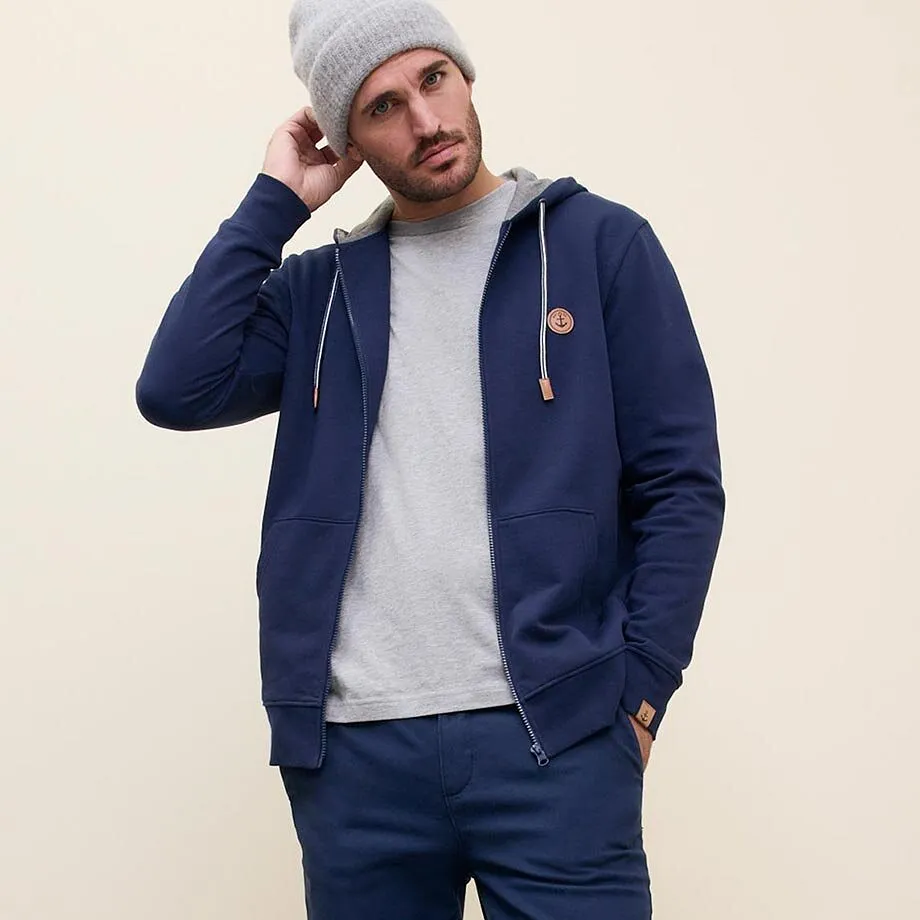Look casual con giacca blu con cappuccio, berretto grigio e maglione chiaro.