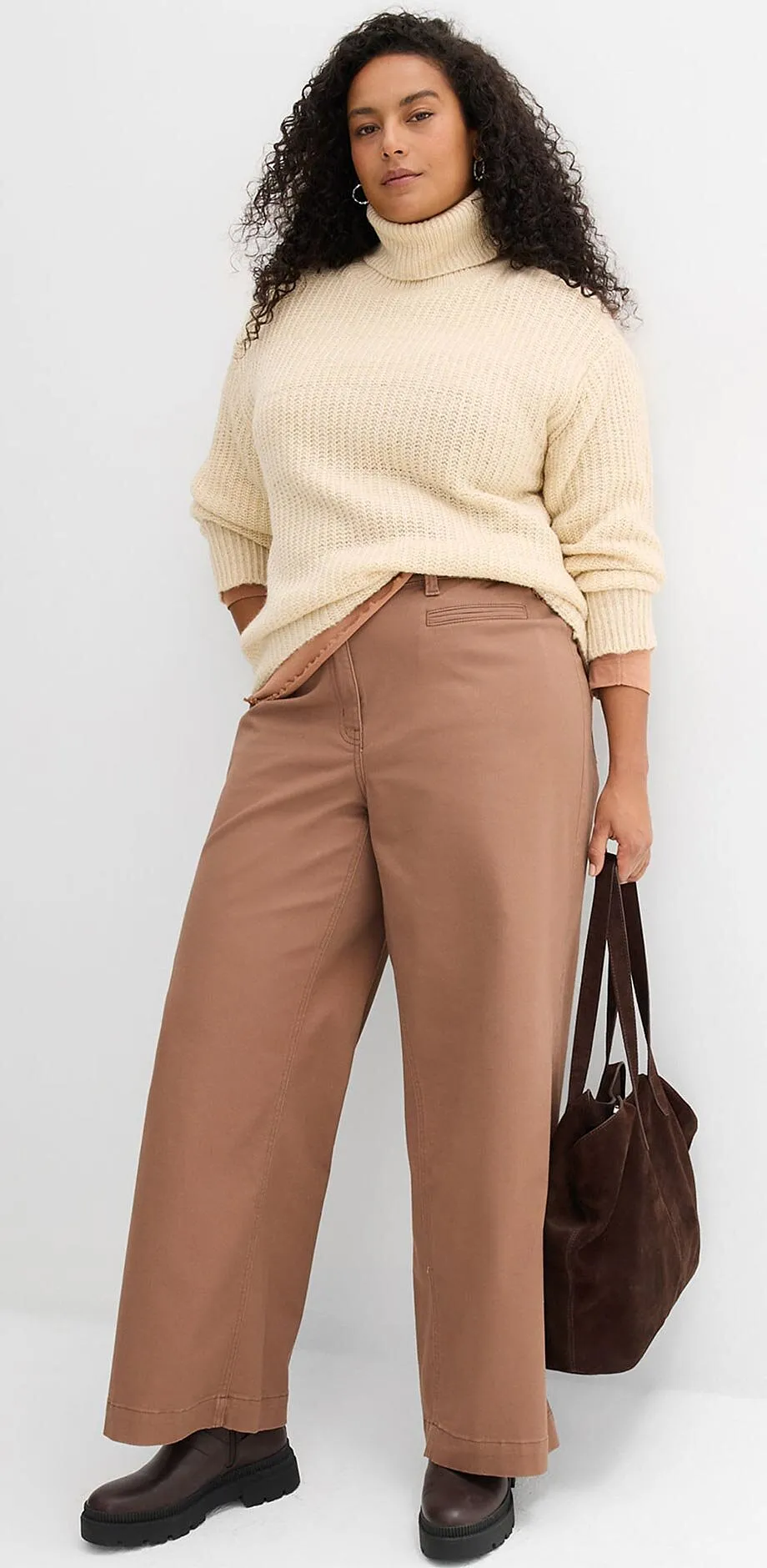 Maglione lavorato a maglia color crema e pantaloni marroni.