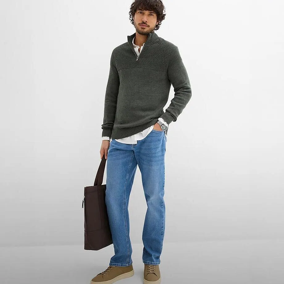 Maglione grigio con cerniera sul collo e jeans blu.