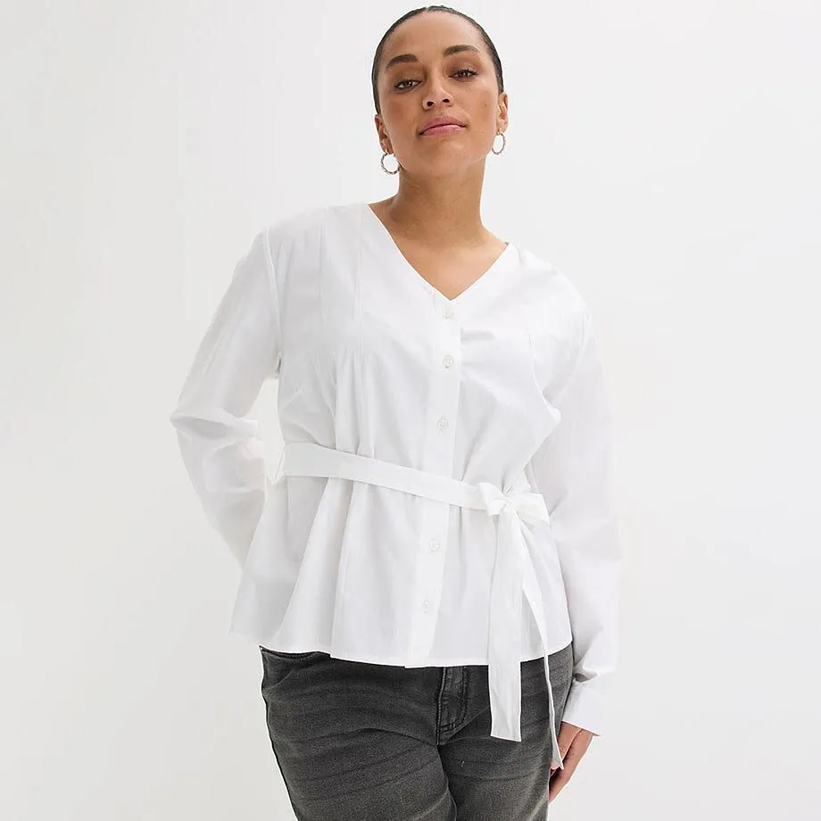 Camicetta bianca con scollo a V e cintura, abbinata a jeans scuri.