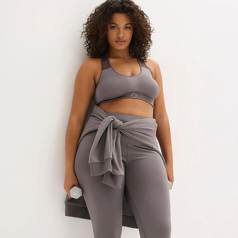 Completo sportivo grigio con reggiseno sportivo e leggings. Maglione annodato intorno ai fianchi.