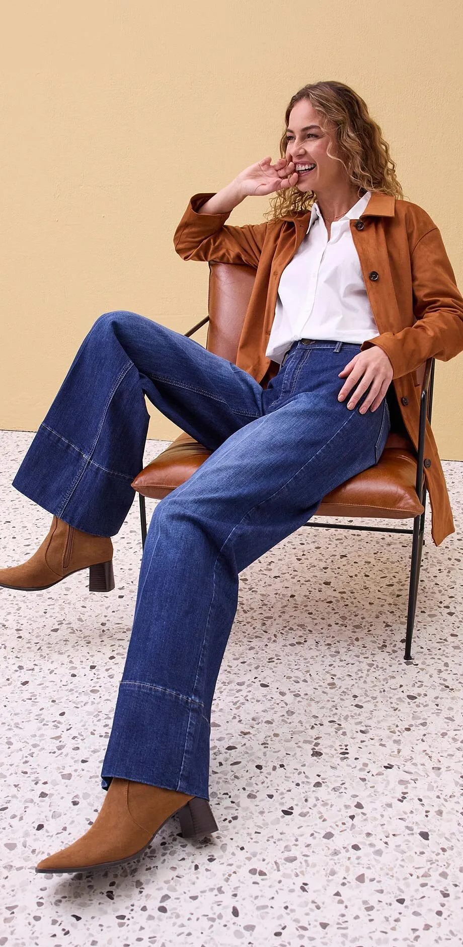 Giacca di pelle marrone, camicia bianca e jeans larghi.