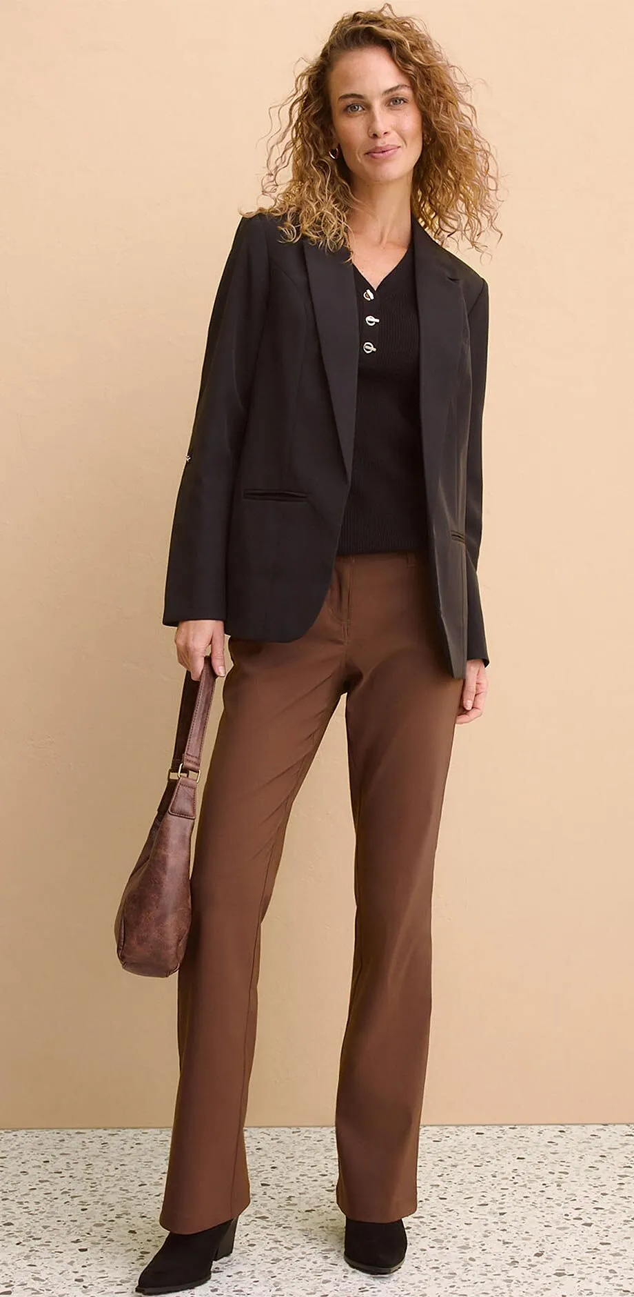Giacca nera su top scuro, abbinata a pantaloni marroni.